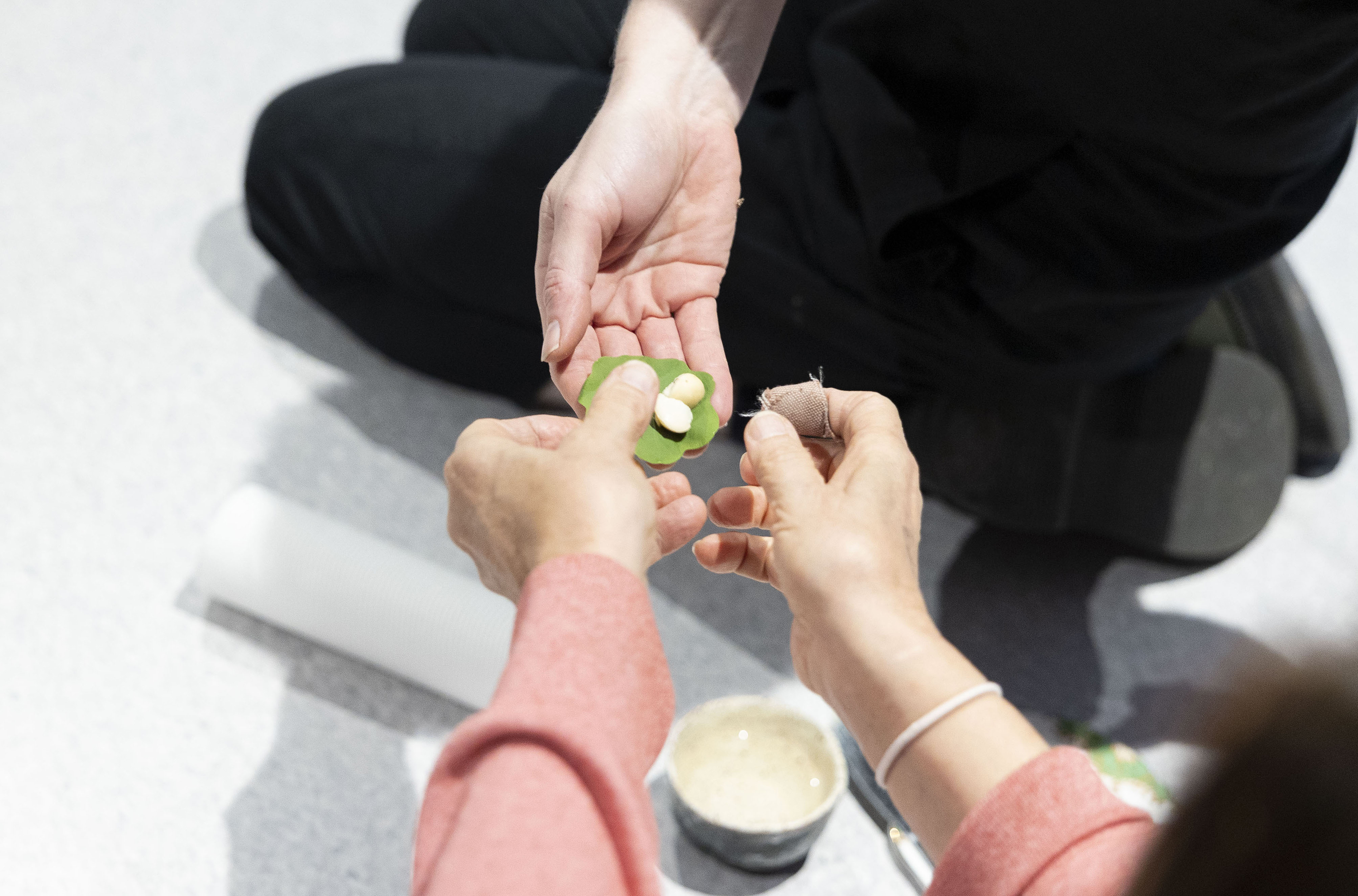 A hand of one person passing macadamia nuts wrapped in a fresh nasturtium leaf to the hands of another